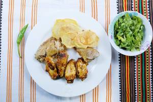 Hähnchenflügel und frittierte Kartoffelscheiben mit grünem Salat auf einer bunten Tischdecke