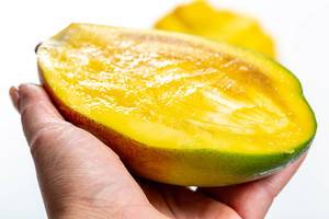 Halbgeschnittene saftige Mango in weiblicher Hand in Nahaufnahme
