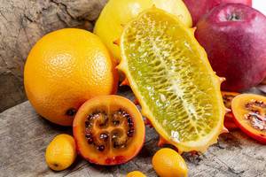 Halbierte Kiwano Horngurke, halbierte Tamarillo, Apfel, Quitte, Orange und Kumquat Früchte auf einem Holztisch