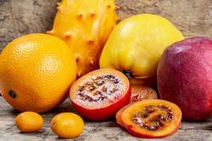 Halbierte Tamarillo, Kumquat Früchte, Orange, Quitte, Kiwano Horngurke und ein Apfel auf einem Holztisch Nahaufnahme