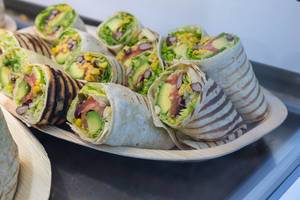 Halbierte Wraps gefüllt mit Avocado, Fisch, Mais und Salat auf Holzplatte