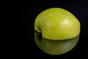 Halbierter grüner Apfel mit Schnittfläche nach unten erscheint durch Reflektion als ganzer Apfel