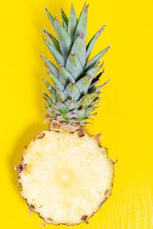 Half ripe pineapple with green leaves on a yellow background