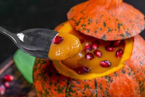 Halloween Konzept - Kürbis mit Kürbispuree gefüllt und Granatafpel mit Löffel closeup