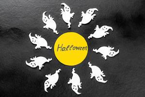 Halloween Schrift in gelbem Papierkreis umgeben von weißen Geistern auf schwarzem Hintergrund