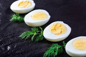 Halves of boiled eggs on a black background with greens