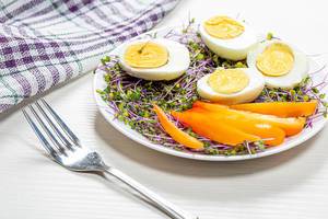 Halves of boiled eggs with micro greens and pieces of bell pepper in a white plate