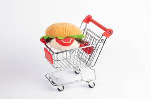 Hamburger aus Stoff in Einkaufswagen vor weißem Hintergrund