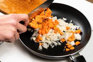 Hand beim Schneiden von Karotten und Zwiebeln in einer Bratpfanne