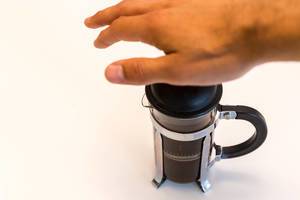 Hand benutzt den Kaffeebereiter und drückt das Sieb in der Glaskanne nach unten, um Kaffee zu kochen