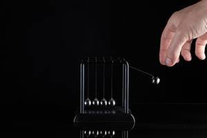 Hand betätigt Kugelstoßpendel der Newton-Wiege vor schwarzem Hintergrund