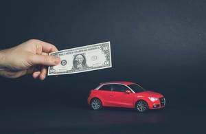 Hand hält Banknote über rotes Auto symbolisiert Sparen und den Kauf eines Autos