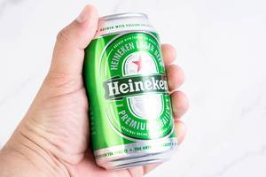 Hand hält das niederländische Dosenbier Heineken in der Hand, vor weißem Hintergrund