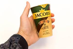 Hand hält die geschlossene Verpackung des Latte Kaffees von Jacobs Krönung mit Baileys aus 100% Arabicabohnen und Alpenmilch