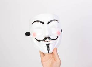 Hand hält die V wie Vendetta-Maske vor weißem Hintergrund, die auch von Anonymous-Aktivisten und der Occupybewegung benutzt wird