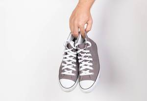 Hand hält ein Paar grau-weiße Sneaker vor weißem Hintergrund