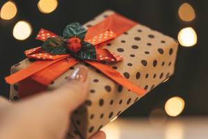Hand hält ein Weihnachtsgeschenk vor Hintergrund im Bokeh-Effekt durch weihnachtliche Girlande