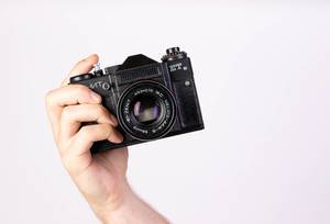 Hand hält eine alte Vintagekamera im Retrostil in die Kamera, vor weißem Hintergrund