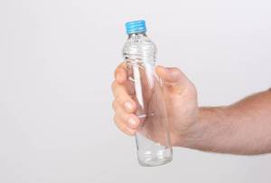 Hand hält eine leere Glasflasche mit Drehverschluss vor weißem Hintergrund