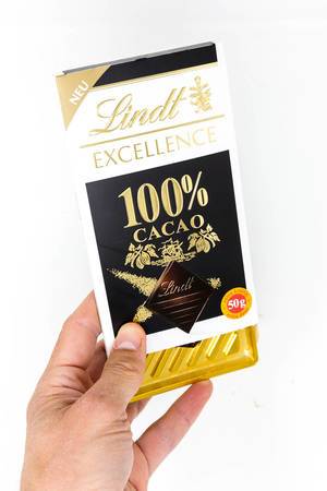 Hand hält eine Lindt Excellence 100 Prozent Kakao Schokoladentafel vor weißem Hintergrund