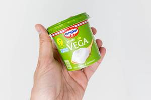 Hand hält eine Packung Creme Vega auf Soja-Basis von Dr. Oetker vor weißem Hintergrund. Dieses Produkt ist eine vegane Alternative zu Crème fraîche zum Kochen und Verfeinern