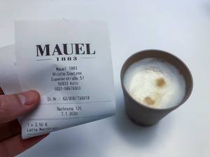 Hand hält einen Beleg für den Kauf von einem Latte Macchiato in einem Café in Köln