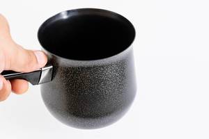 Hand hält einen dunklen Topf zum Kaffeekochen
