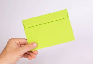 Hand hält einen grünen Umschlag vor weißem Hintergrund