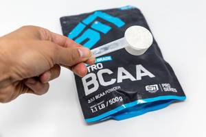 Hand hält einen Messlöffel mit Aminosäure-Pulver Nitro BCAA von ESN über die wiederverschließbare Verpackung