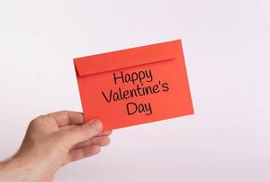Hand hält einen roten Umschlag vor weißem Hintergrund, mit der Aufschrift "Happy Valentine