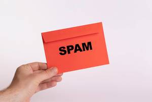 Hand hält einen roten Umschlag vor weißem Hintergrund, mit der Aufschrift "Spam"