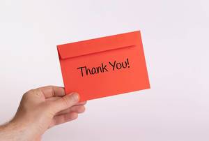 Hand hält einen roten Umschlag vor weißem Hintergrund, mit der Aufschrift "Thank you" - Dankeschön