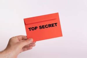 Hand hält einen roten Umschlag vor weißem Hintergrund, mit der Aufschrift "Top Secret" - Streng Geheim