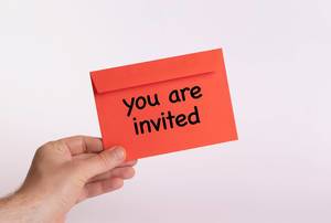 Hand hält einen roten Umschlag vor weißem Hintergrund, mit der Aufschrift "you are invited" - Du bist eingeladen