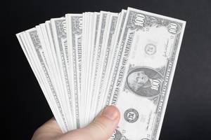 Hand hält Fächer aus 100 Dollar Noten vor schwarzem Hintergrund
