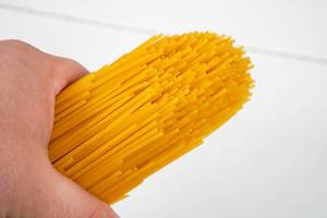 Hand hält frische, rohe Spaghetti vor einem weißen Holzhintergrund