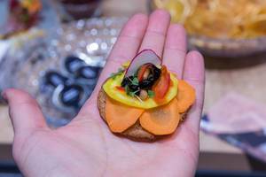 Hand hält kleinen Brotsnack mit heimischem Gemüse und exotischem Obst: Möhrenscheiben, Mango, Radieschen und Kräuter als Brotbelag