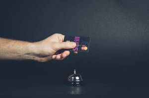 Hand hält Kreditkarte über Hotelglocke symbolisiert Bezahlen von Hotelzimmer mit Kreditkarte