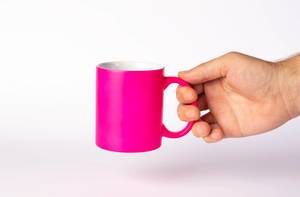 Hand hält leuchtend pinke Kaffeetasse vor weißem Hintergrund