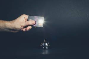 Hand hält Mastercard Kreditkarte über silberne Hotelklingel vor dunklem Hintergrund