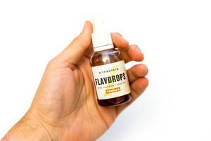 Hand hält MyProtein Flavdrops mit Geschmacksrichtung Vanille vor weißem Hintergrund