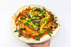 Hand hält tiefgefrorene Pizza mit gegrilltem Gemüse und frischem Brokkoli vor weißem Hintergrund