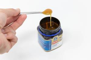 Hand holding a spoon of liquid honey over a  Manuka honey jar