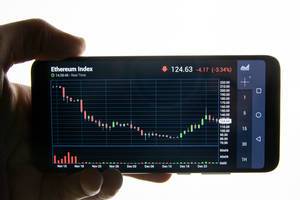 Hand holding smart phone with Ethereum chart on screen
