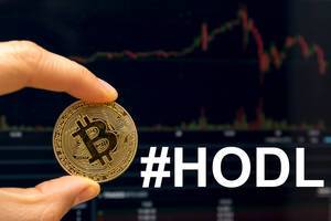 Hand holds a golden bitcoin next to the hashtag #HODL