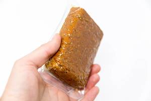 Hand holds a package of smoked tofu with sesame and almonds. Organic and vegan product by Tukan