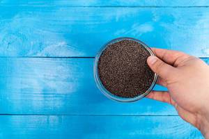 Hand holds Bowl with Poppy Seeds above blue wooden background (Flip 2020)