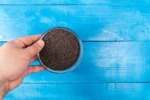 Hand holds Bowl with Poppy Seeds above blue wooden background