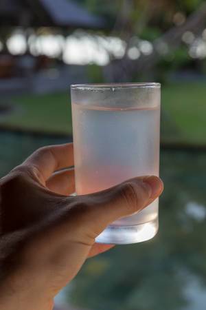 Hand holds cold Coconut Water in a Glas in front of blurred background at Constance Ephelia Resort in Mahé, Seychelles
