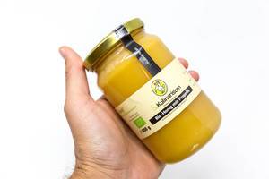 Hand holds extraordinary organic honey with propolis by "Die Kulinaristen", cold spun, in a glass